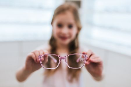 Una niña sostiene un par de gafas rosas en sus manos.