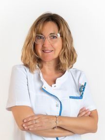 Una mujer que lleva gafas y un uniforme blanco está de pie con los brazos cruzados.