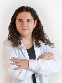 Una mujer con una bata de laboratorio blanca está de pie con los brazos cruzados.