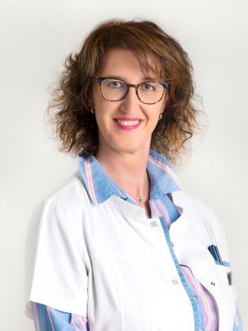 Una mujer que lleva gafas y una bata blanca sonríe para la cámara.