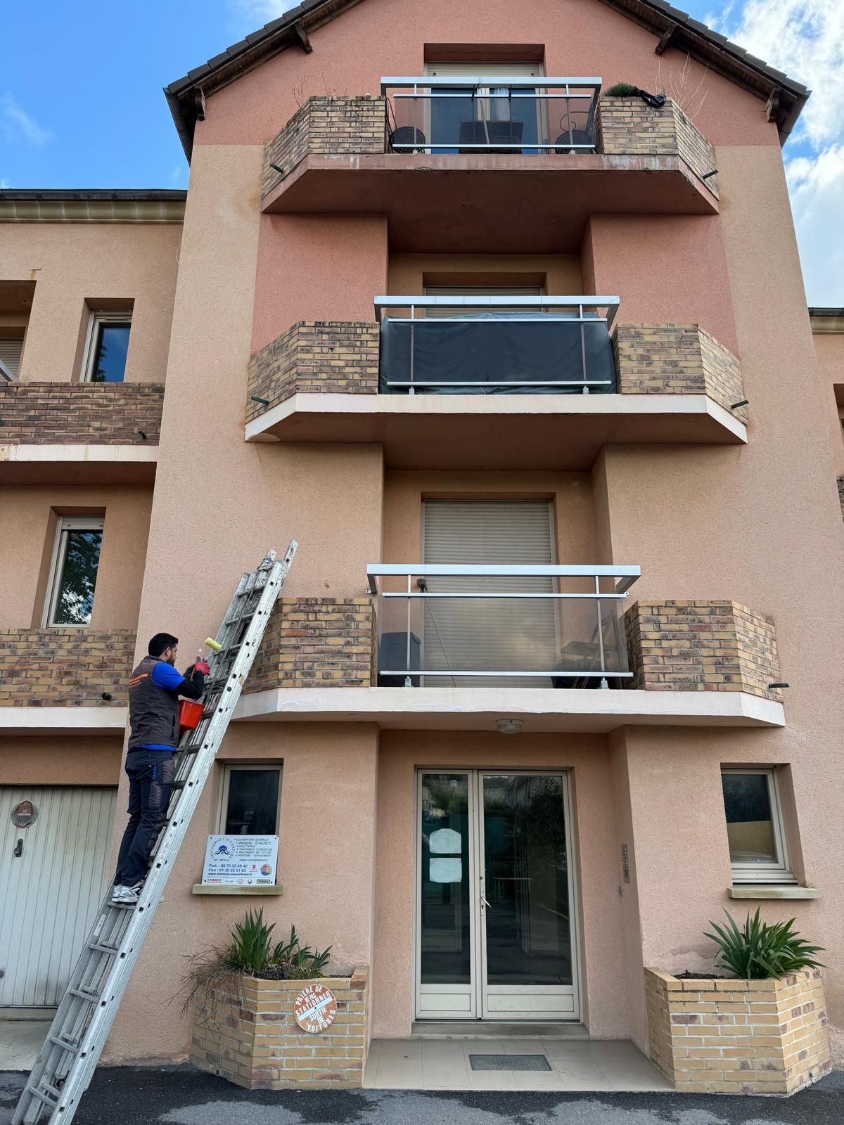 Un homme sur une échelle contre un balcon effectue des travaux de ravalement sur une façade