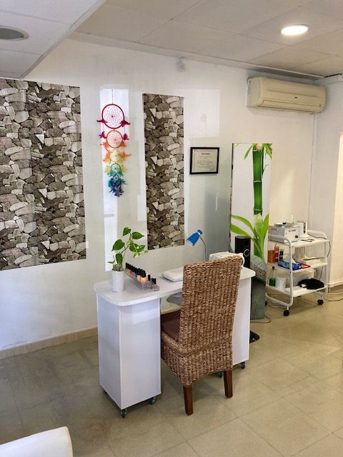 Interior de salón de uñas con estación de manicura, decoración de bambú y pared con patrón de piedra.