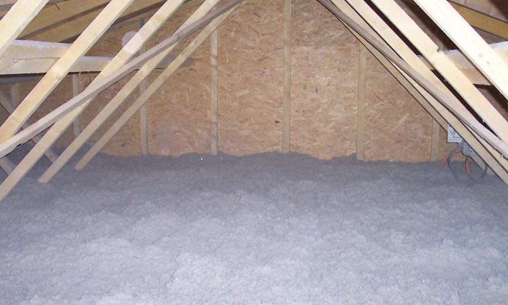 Combles avec charpente en bois, murs en panneaux OSB et isolation grise au sol.