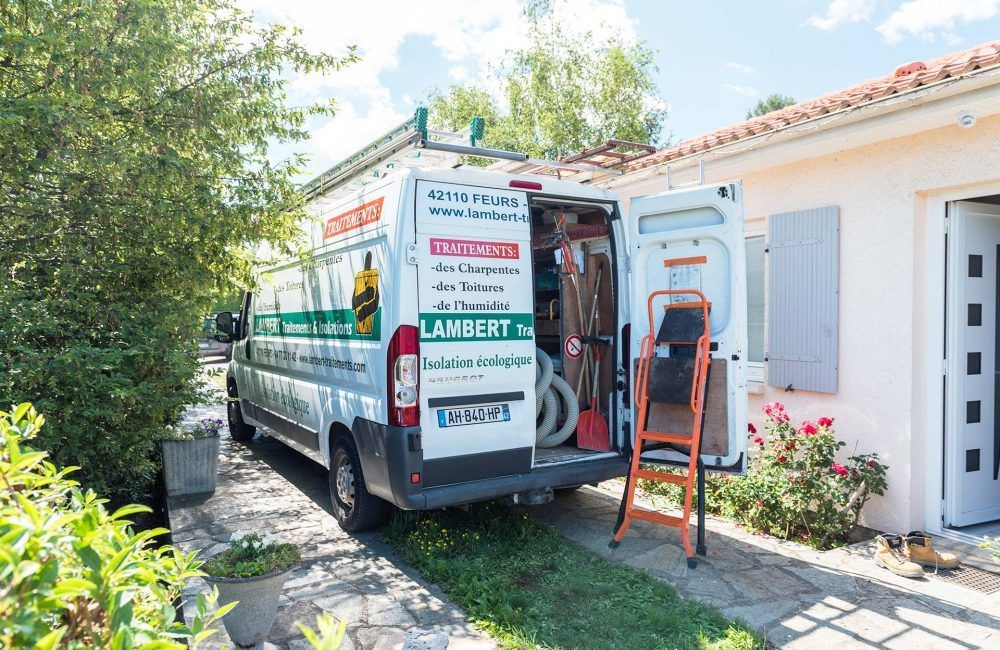 Une camionnette blanche est garée devant une maison, portes ouvertes, outils visibles. Une échelle orange est appuyée contre la camionnette.