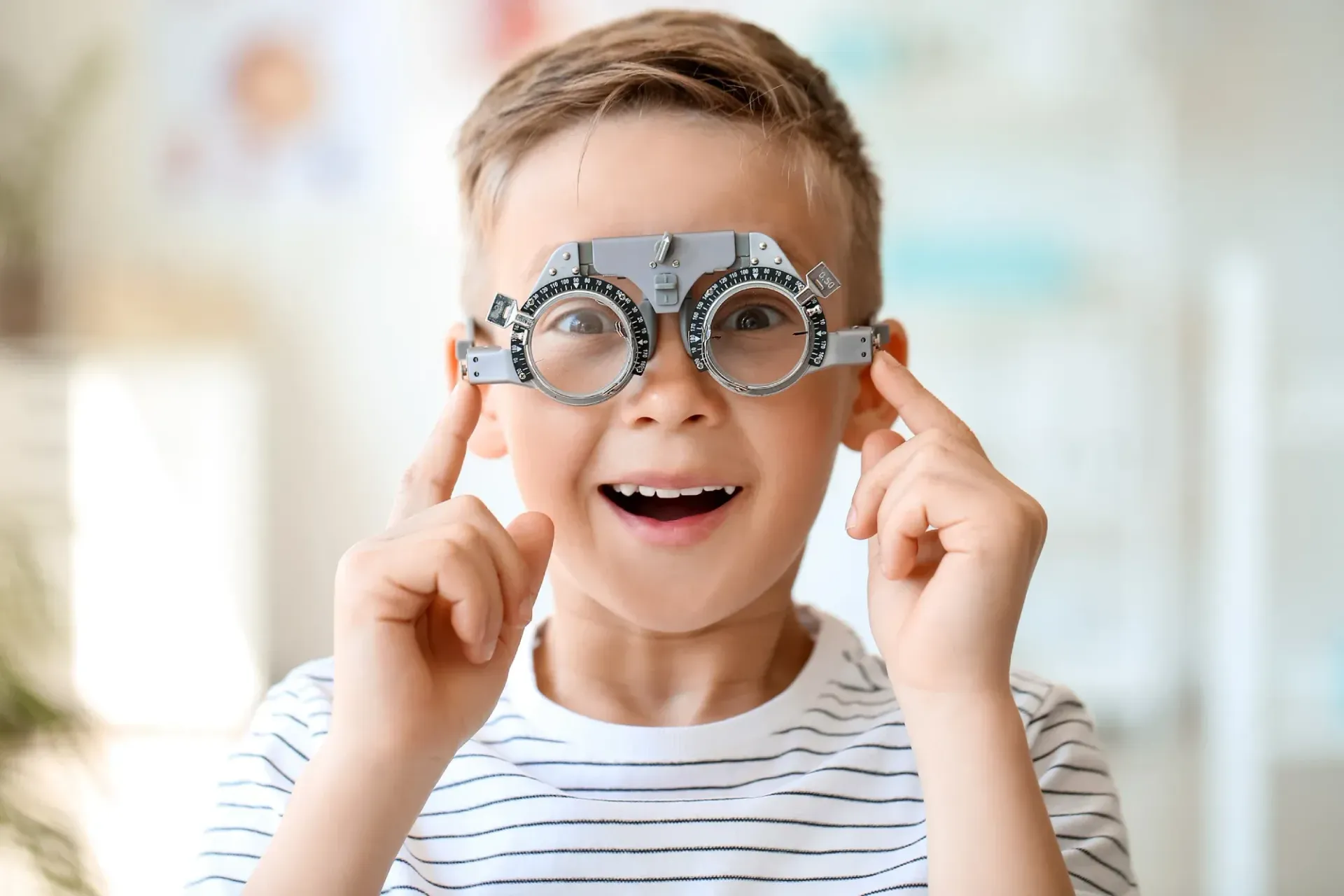 Niño que usa gafas con montura de prueba, sonriendo durante un examen de la vista.