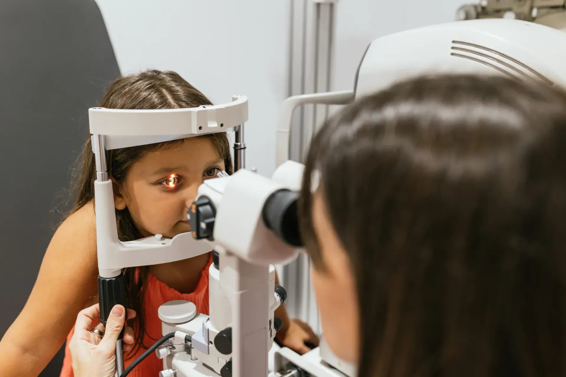 Una niña se somete a un examen de los ojos por parte de una persona que utiliza una máquina de examen ocular.