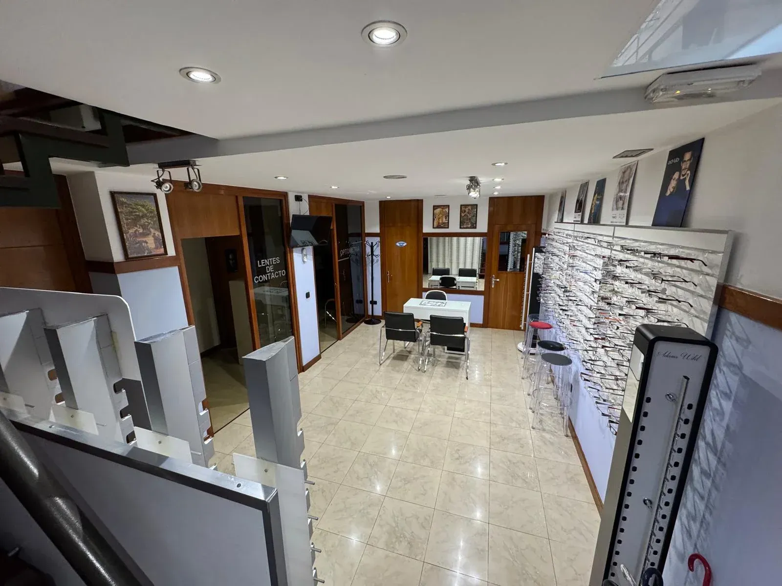 Interior de un consultorio de optometría con gafas en exhibición, una mesa y sillas y una escalera.