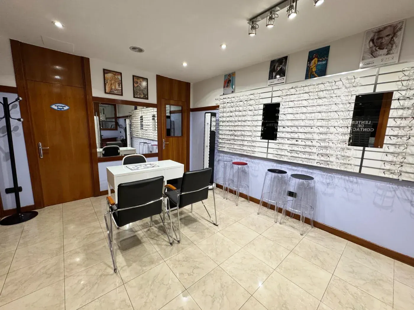 Interior de una tienda de óptica con expositores de gafas, sillas y una mesa.