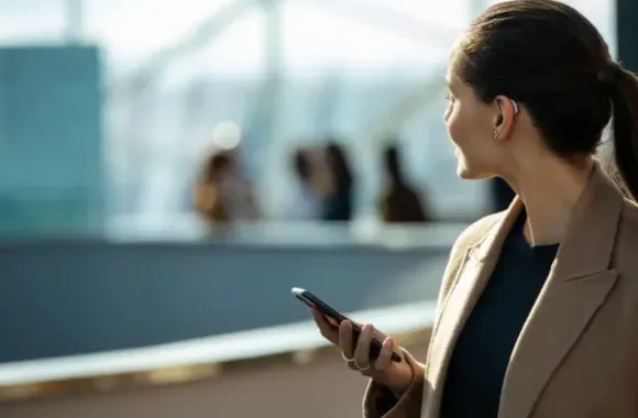 Mujer con audífono detrás de la oreja, cola de caballo, cabello castaño, fondo oscuro.
