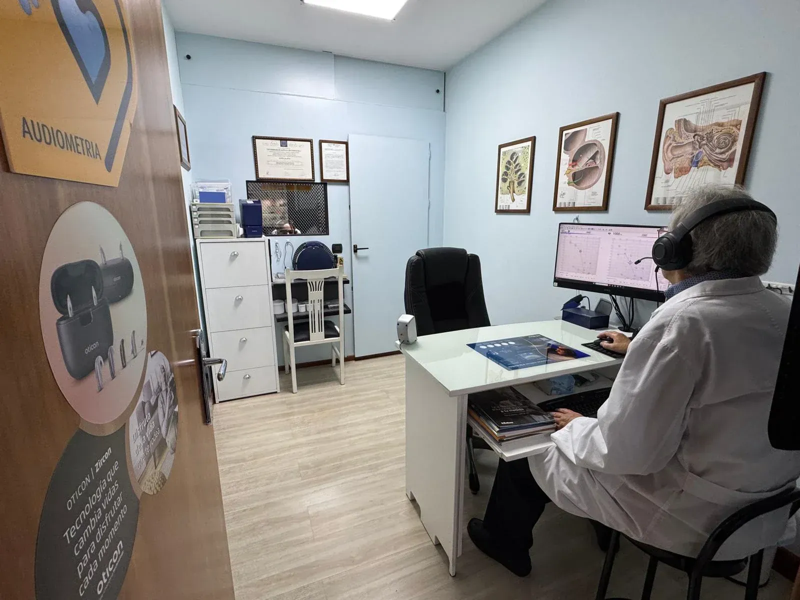 Una persona con bata de laboratorio está sentada en un escritorio en una oficina. Está usando una computadora.