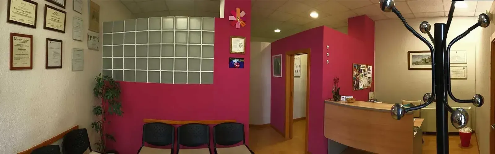 Una sala de espera con paredes rosas y un perchero negro.