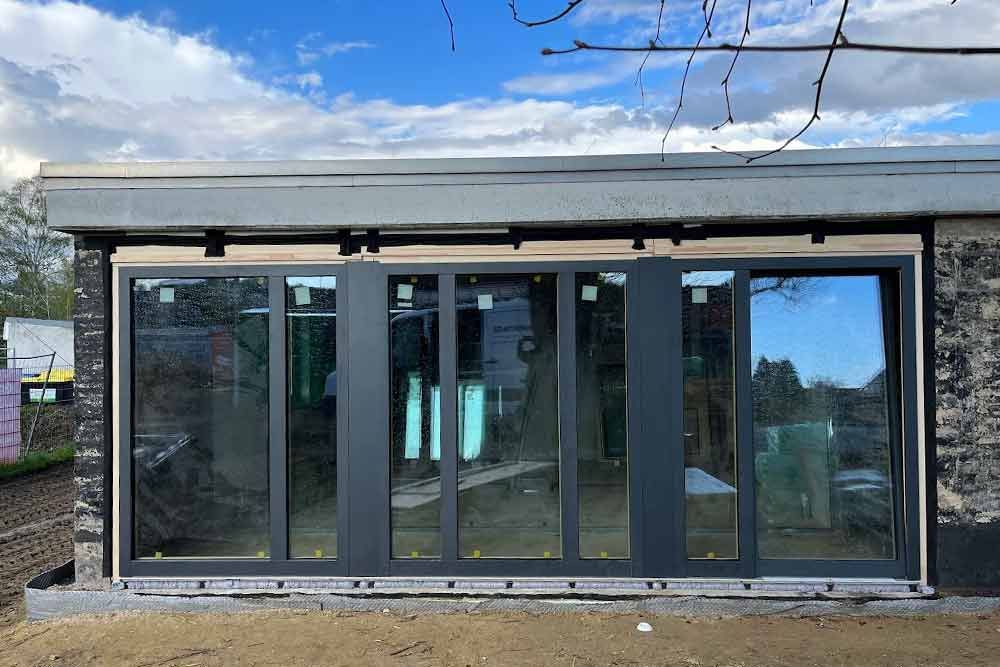 Schwarz gerahmte Glas-Falttüren an einem Gebäude. Außenansicht mit bewölktem Himmel, Erde und Ziegeln.