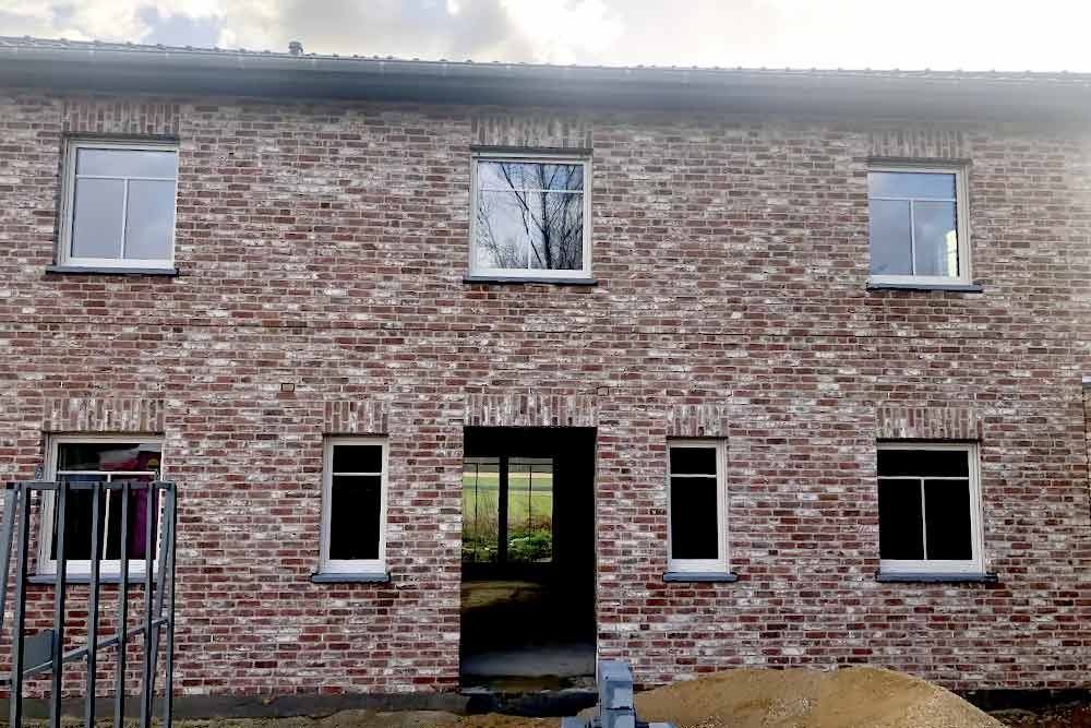 Außenansicht eines Backsteingebäudes mit Fenstern und einer offenen Tür.