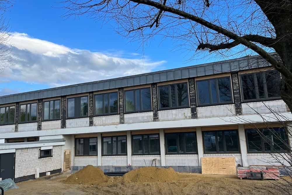 Gebäudeaußenseite mit Fenstern und Baumaterialien unter blauem Himmel.