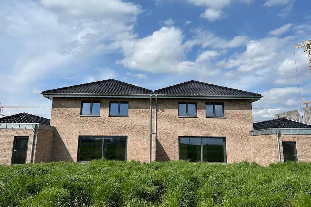 Zwei Backstein-Stadthäuser mit schwarzen Dächern und Fenstern vor einem blauen Himmel.