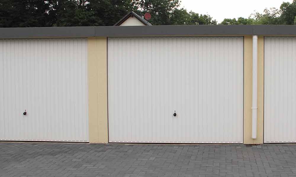 Drei weiße Garagentore mit hellbrauner Verzierung, auf Pflastersteinen.