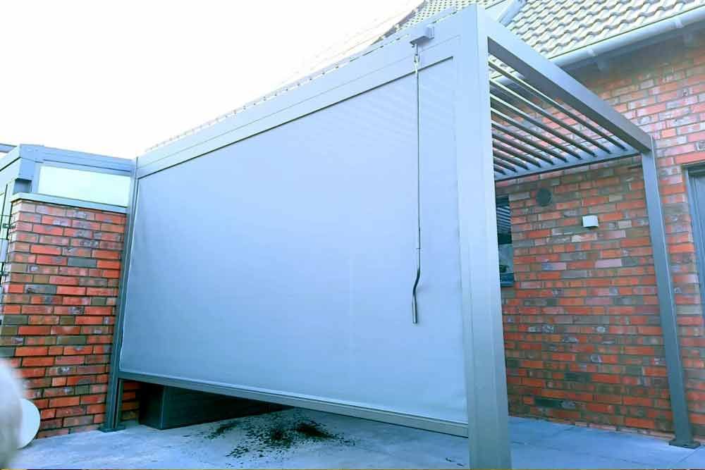 Graue Außenmarkise neben einer Backsteinmauer und einem Gebäude mit Glasfenstern.