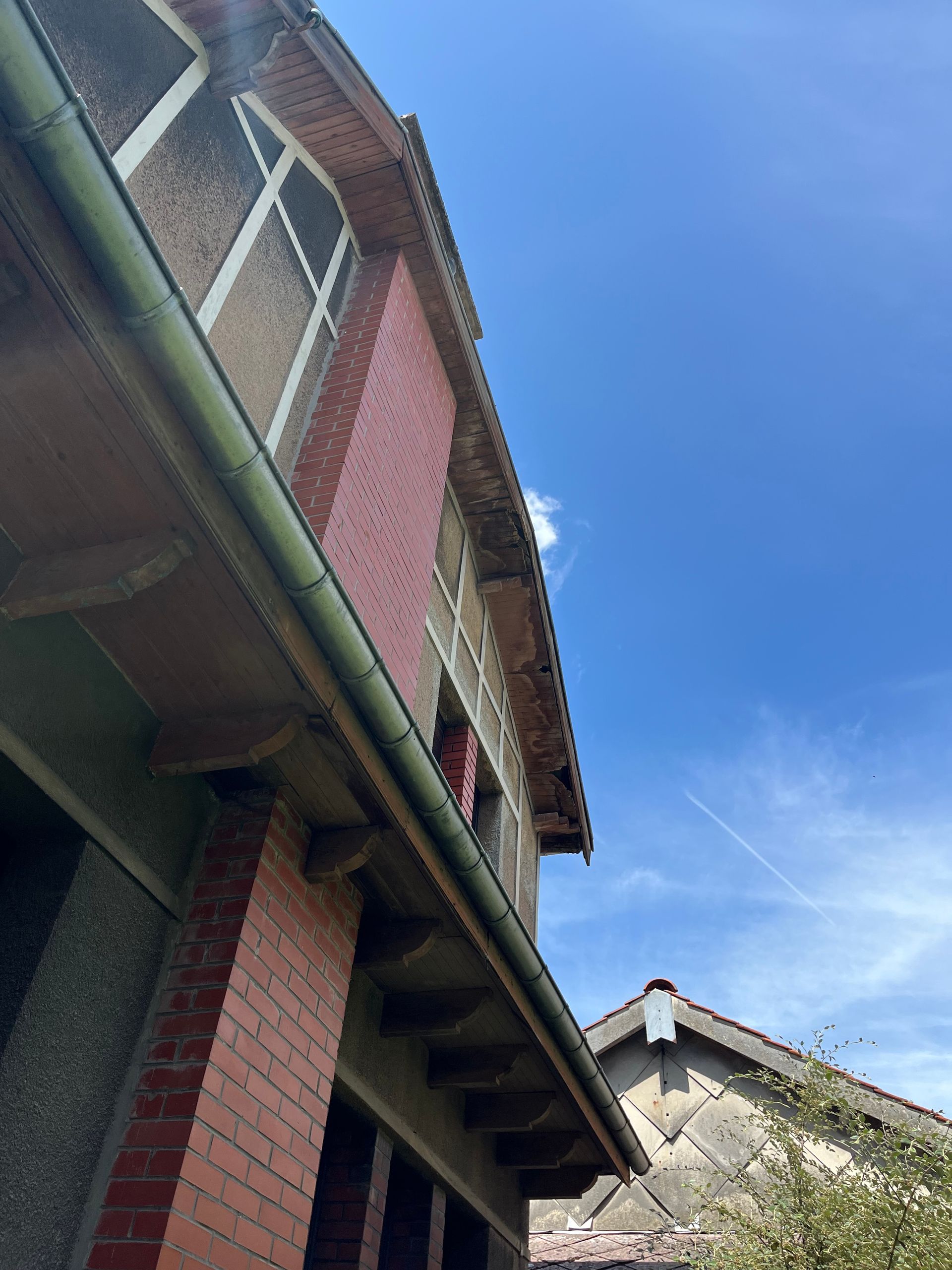 Maison en briques rouges aux fenêtres à encadrement blanc et aux avant-toits saillants se détachant sur un ciel bleu