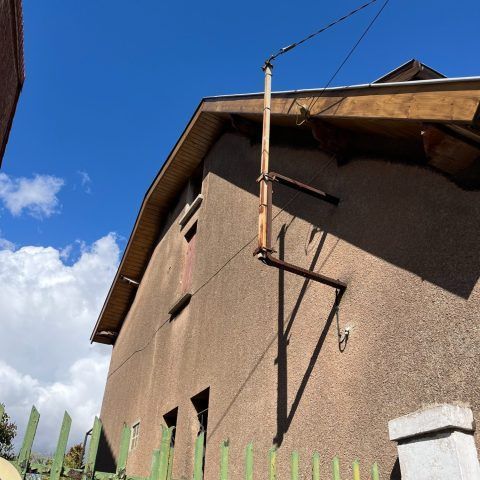 Maison en stuc brun avec toit en pente, descente de gouttière et ciel bleu au-dessus