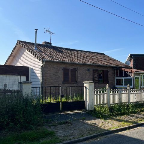 Maison de plain-pied en briques, toit de tuiles, clôture blanche et ciel bleu azur.