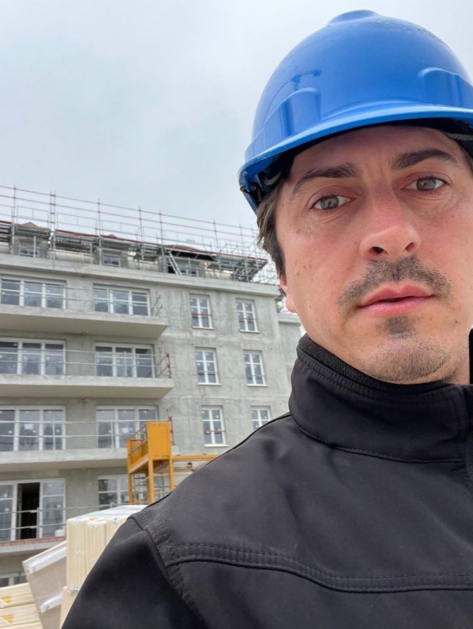 Un ouvrier portant un casque de chantier bleu prend un selfie sur un chantier de construction .