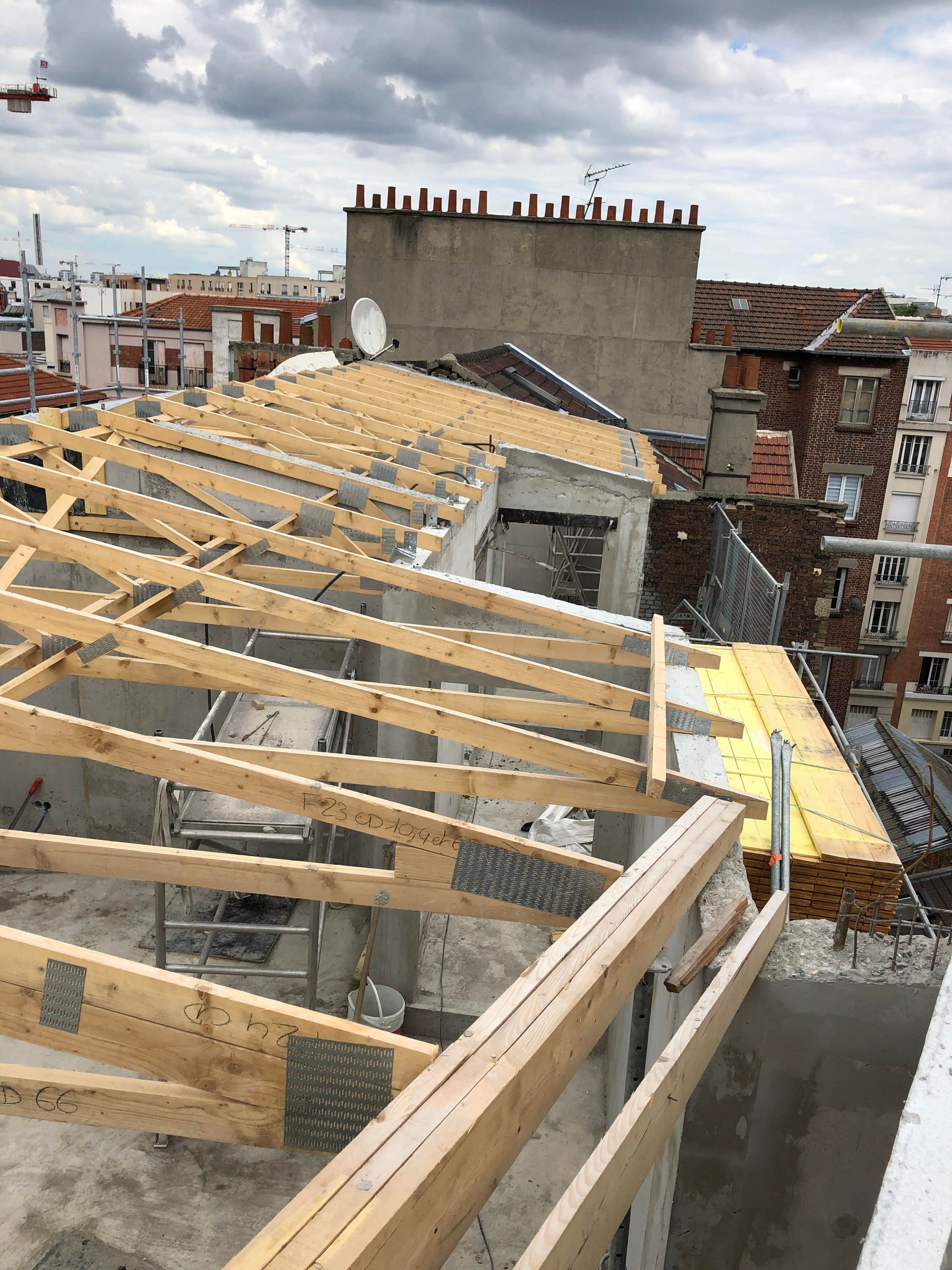 Toiture en construction avec poutres en bois apparentes et bâtiments en briques en arrière-plan