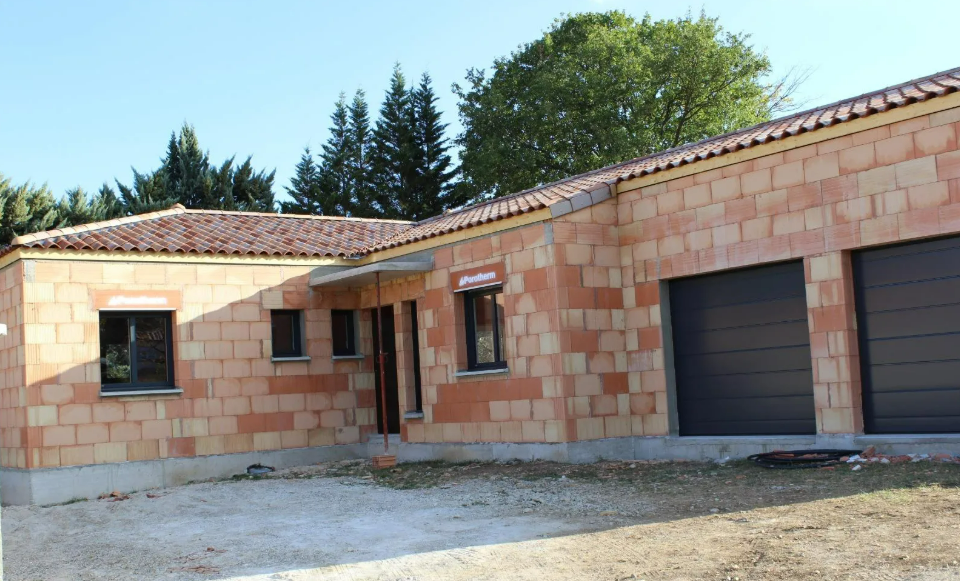 Maison construite en briques avec portes de garage, des fenêtres et un toit en tuiles rouges.