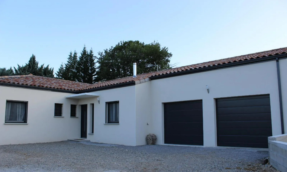 Maison blanche avec toit en tuiles,deux portes de garage noires et allée en gravier.