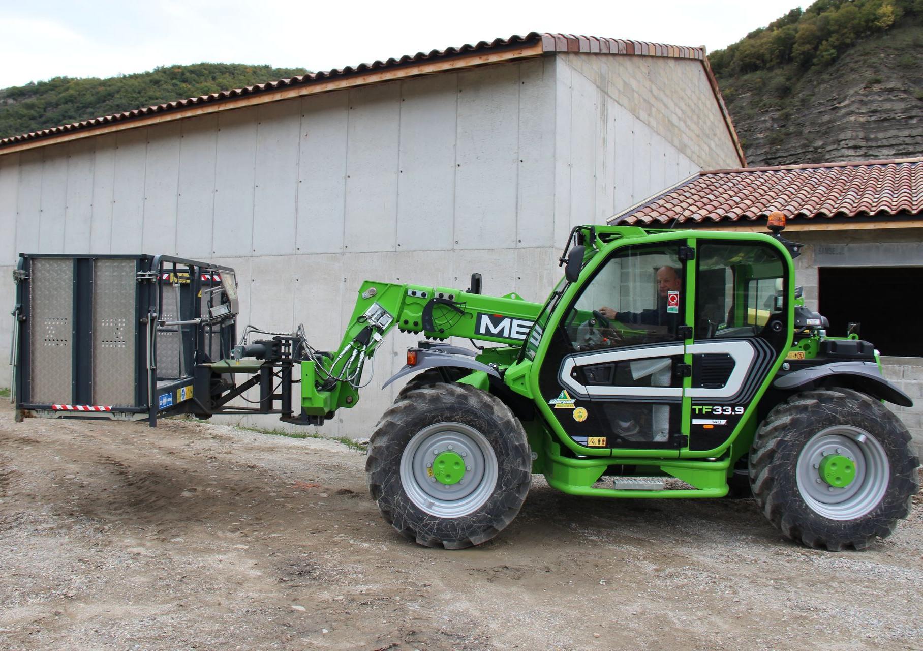 Chariot télescopique vert soulevant une caisse métallique.