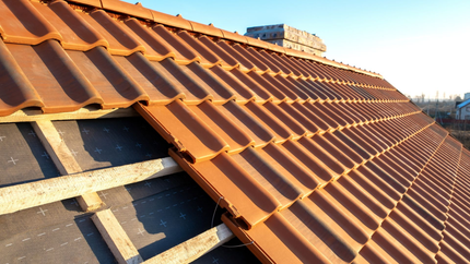 Pose de tuiles orange sur une toiture en bois.
