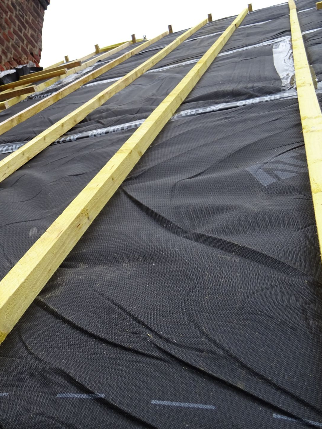 Sous-couche de toiture noire installée sur des chevrons, avec des tasseaux de bois cloués sur le dessus.