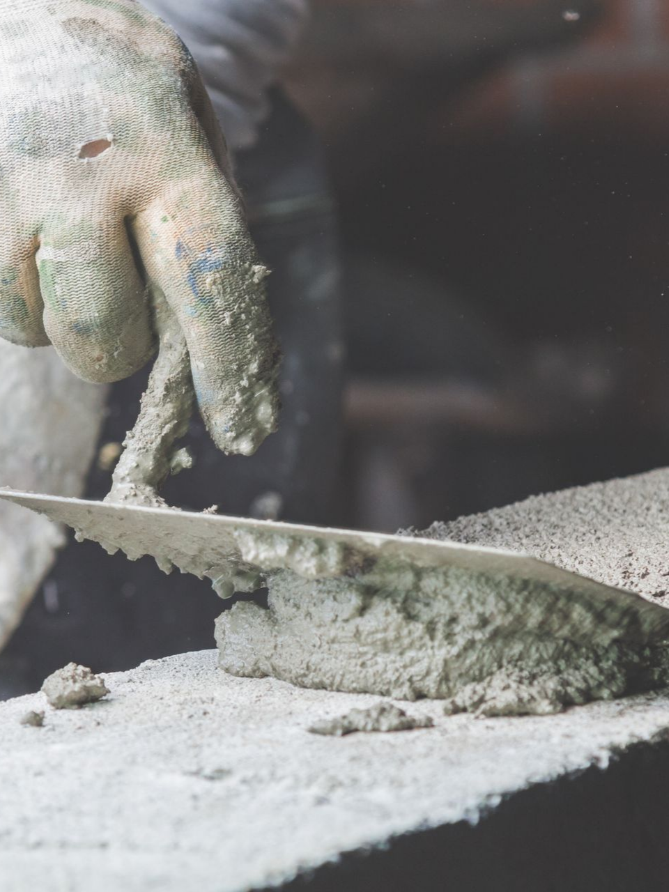 Une main gantée utilise une truelle pour appliquer du ciment sur une surface.