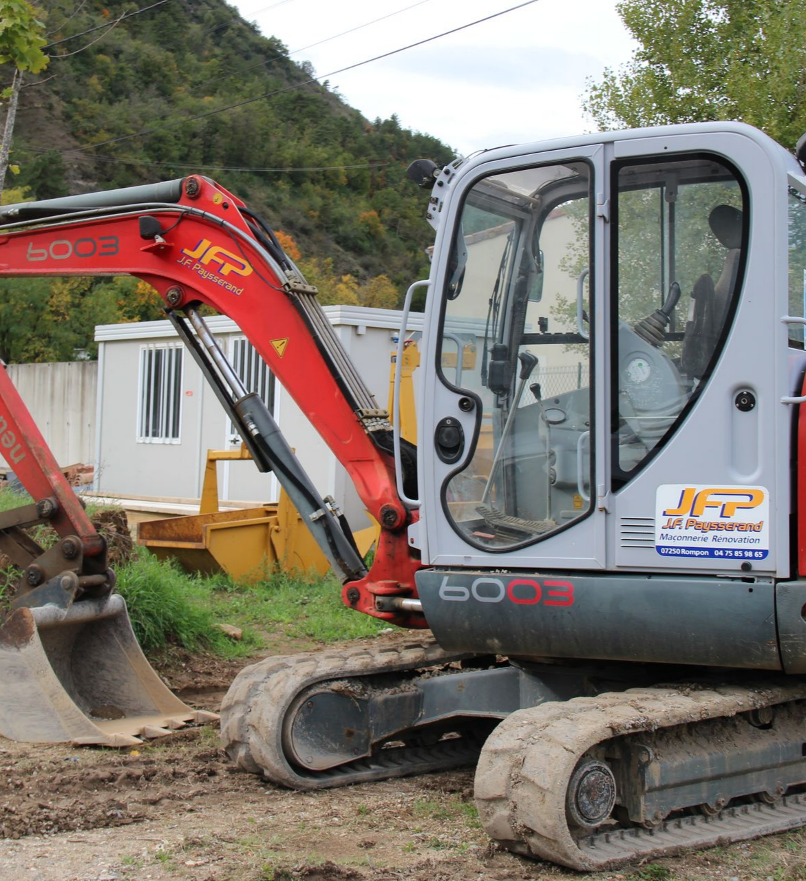 Excavatrice rouge et grise sur un sol boueux.