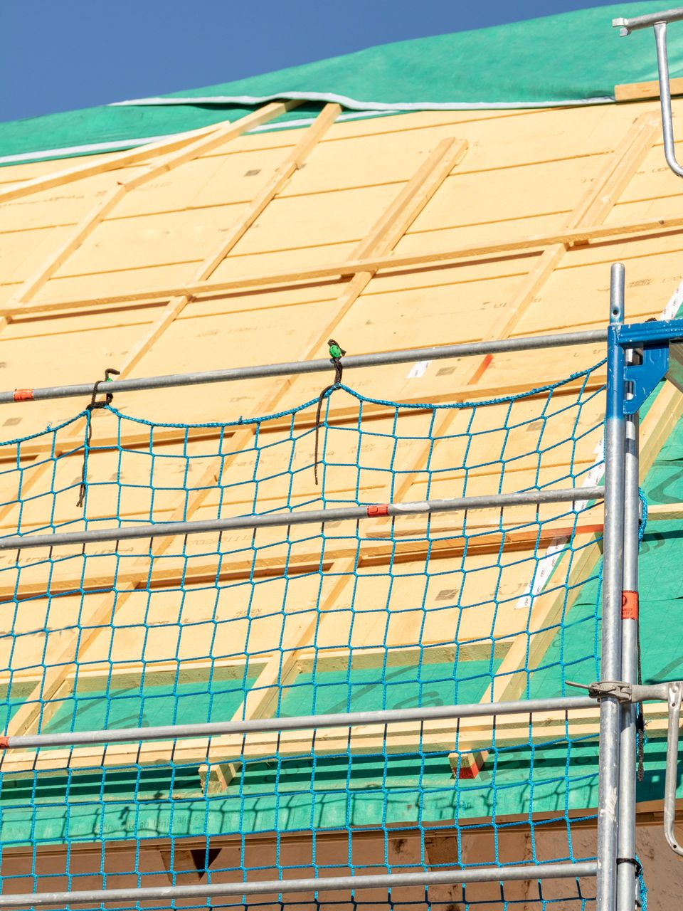 Filet de sécurité installé sur le toit d'un chantier d'isolation. Bâche verte et échafaudage métallique bleu.