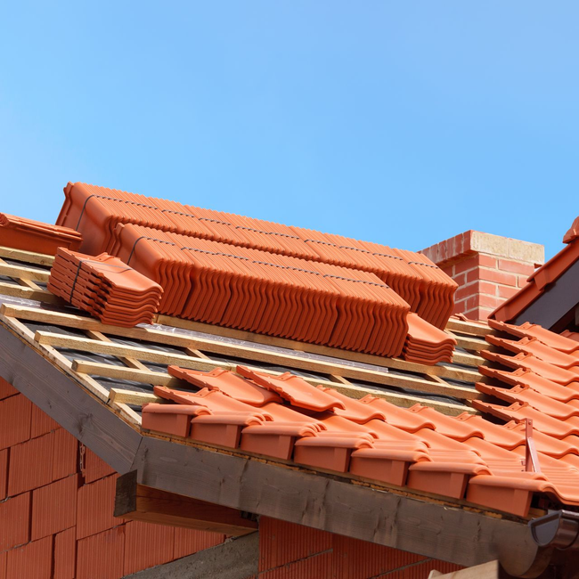 Construction du toit avec des tuiles orange et des piles de tuiles neuves.