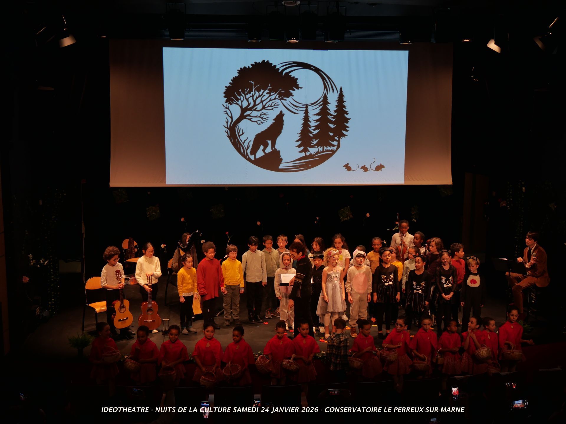 Des enfants sur scène, devant un décor représentant un loup hurlant à la lune.