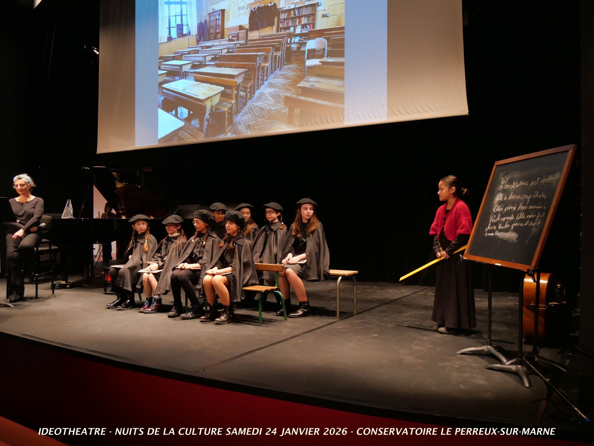 Des élèves vêtus de capes se produisent sur scène devant un tableau noir et l'image projetée d'une salle de classe.