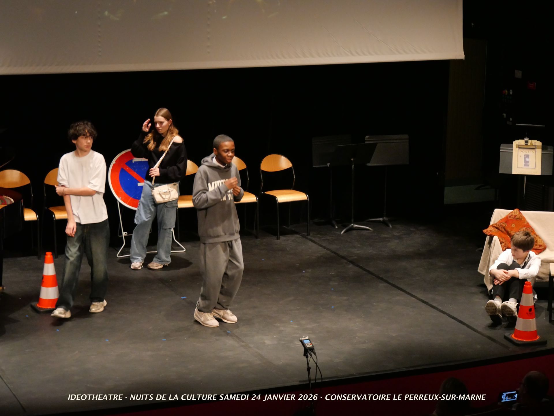 Quatre personnes sur scène : un garçon et une fille près d'un panneau d'interdiction de stationner
