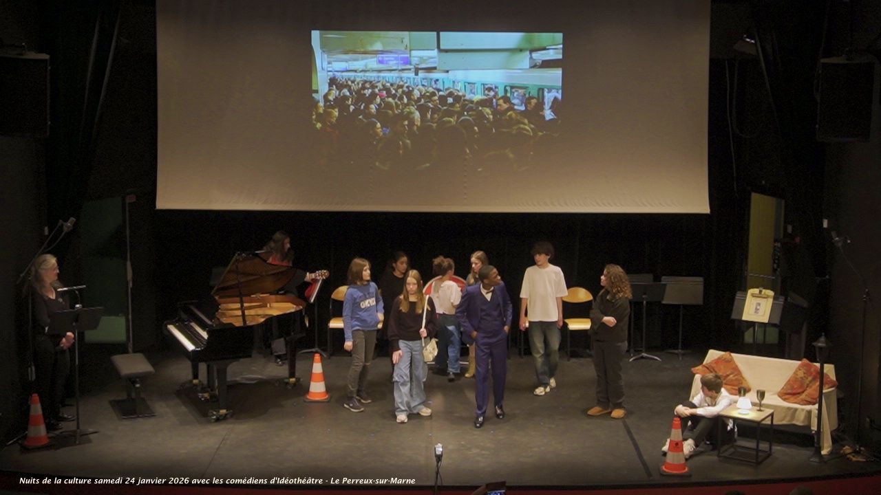 Un groupe de personnes se tient sur une scène, avec un piano et un grand écran montrant une foule.