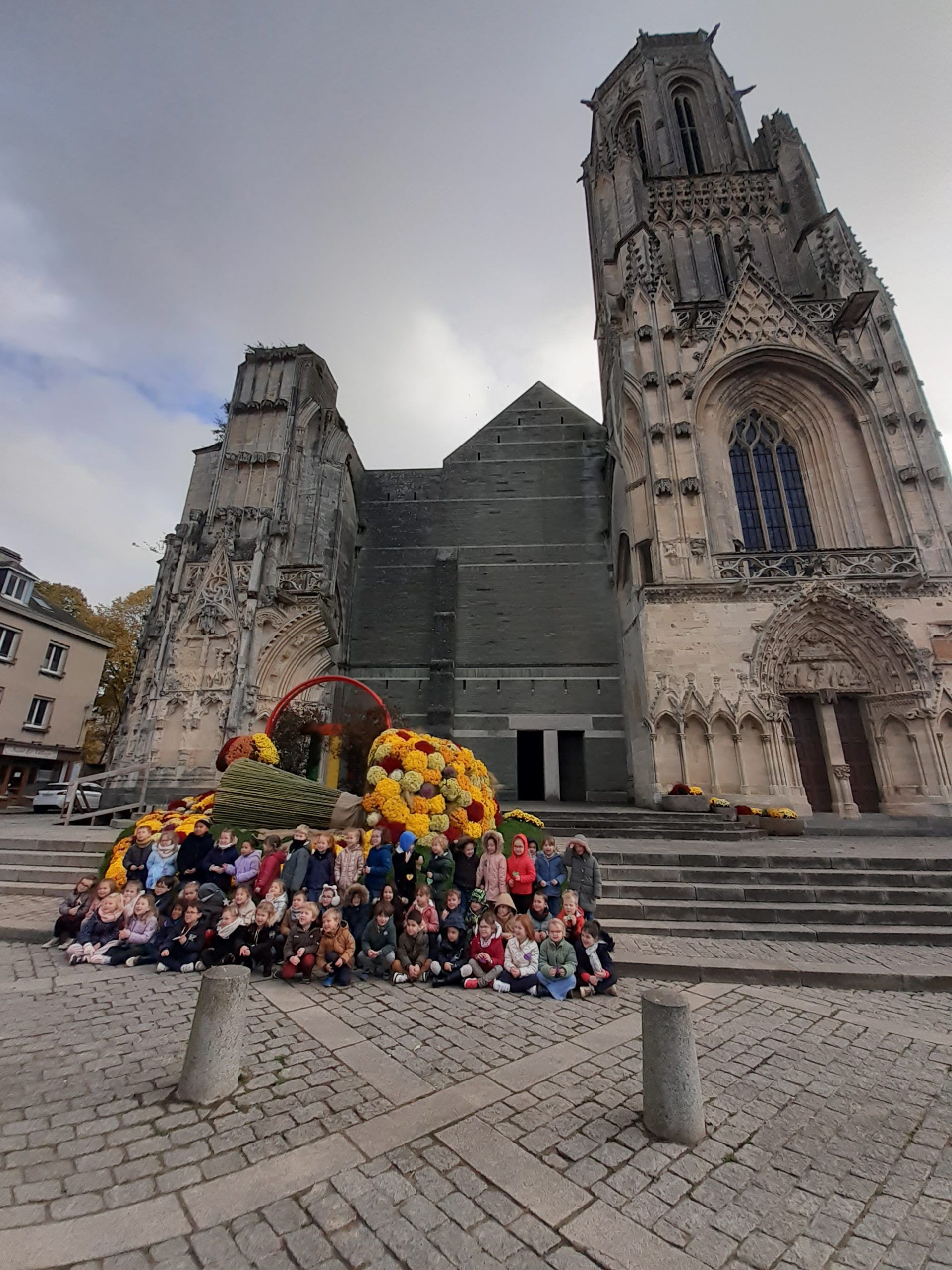 Groupe posant devant une cathédrale historique en pierre, avec de magnifiques compositions florales au premier plan.