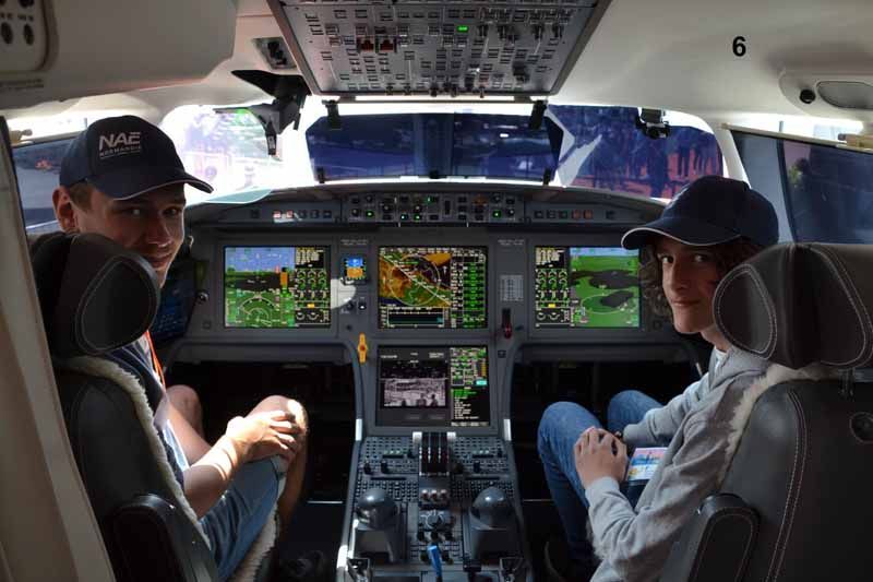 Intérieur du cockpit avec deux personnes assises, face à l'avant, au milieu d'écrans de vol et de commandes illuminés.