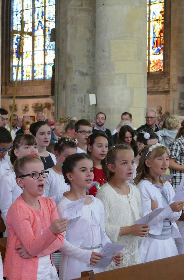 Des enfants chantent en lisant des partitions dans une église, avec des vitraux en arrière-plan.