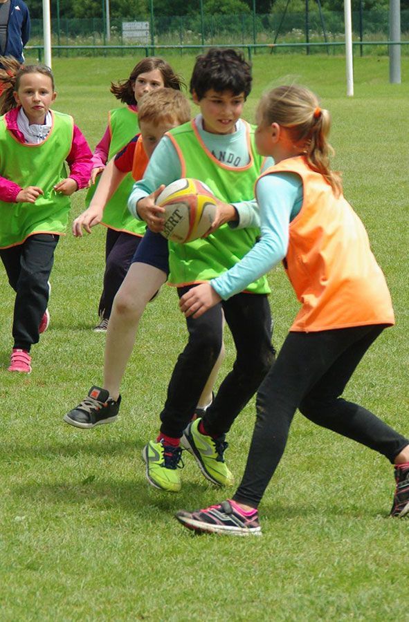 Des enfants jouent au rugby sur un terrain herbeux, l'un d'eux tenant un ballon tandis que d'autres plaquent à proximité.