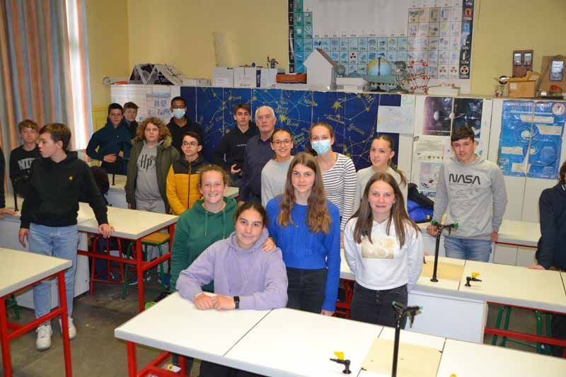 Des élèves debout dans une salle de classe, avec des tables au premier plan et des affiches au fond.