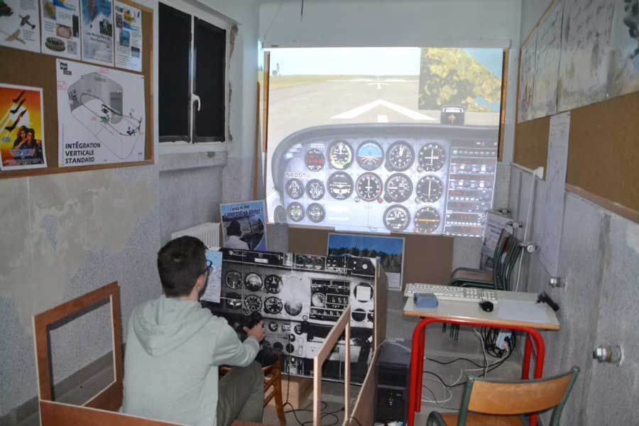 Une personne assise dans le cockpit d'un simulateur de vol, face à un tableau de bord projeté dans une petite pièce