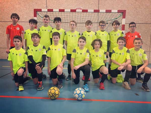 Une équipe de jeunes joueurs de soccer en salle pose devant un but, portant des maillots jaune fluo et orange.