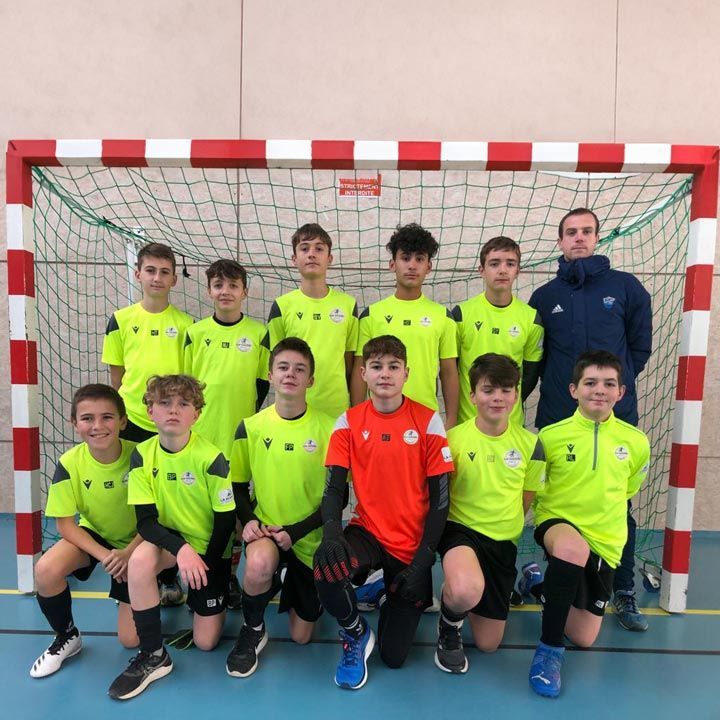 Une équipe de jeunes footballeurs pose en uniformes jaune fluo et orange devant un but en intérieur.