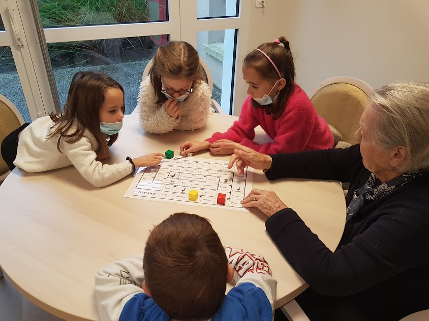 Cinq personnes jouent à un jeu de société autour d'une table dans une pièce lumineuse.