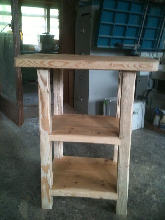 Petite table ou tabouret en bois brut avec étagères, dans un garage ou un atelier.