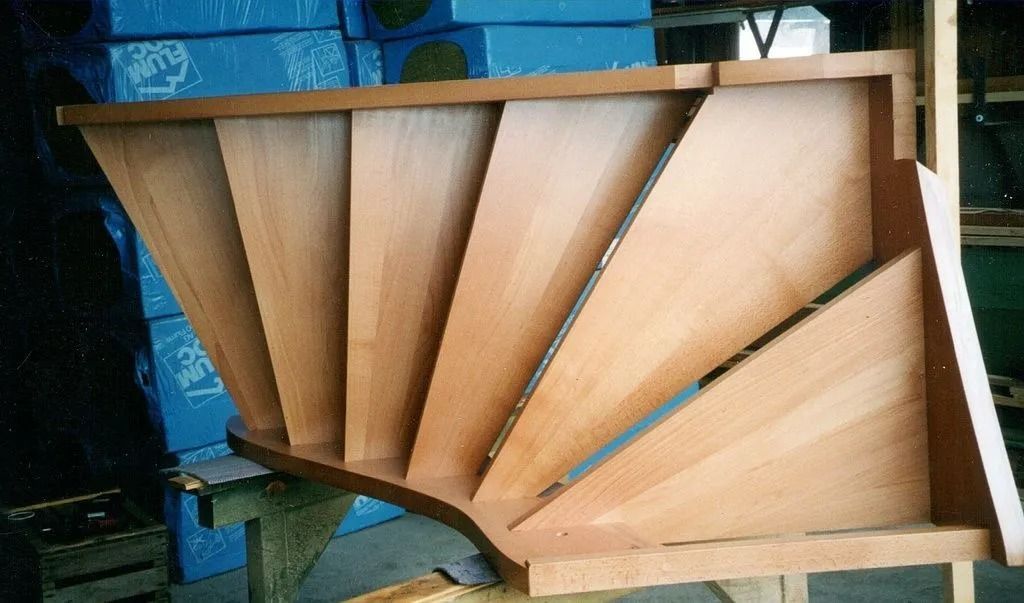 Limon d'escalier en bois en forme d'éventail avec supports triangulaires appuyé contre un mur bleu dans un atelier